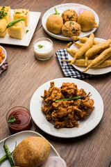 Indian Tea time snacks  in group includes Veg Samosa, Kachori/kachaudi, aloo bonda, khaman dhokla, bread, onion,chilli and moong pakora/pakoda/bhaji/bhajji/Bhajiya/bajji with sauces, selective focus