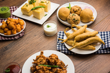 Indian Tea time snacks  in group includes Veg Samosa, Kachori/kachaudi, aloo bonda, khaman dhokla, bread, onion,chilli and moong pakora/pakoda/bhaji/bhajji/Bhajiya/bajji with sauces, selective focus