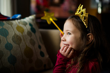 A smiling little girl in window light wears a golden crown and wand