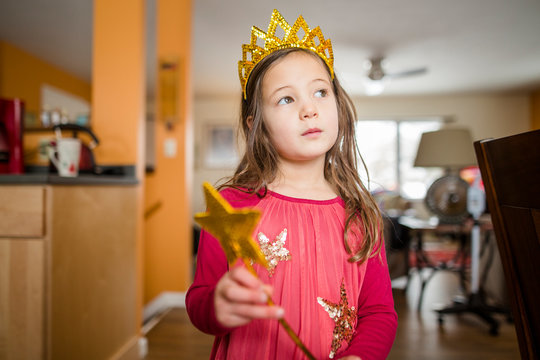 A little girl with a serious expression wears a crown and fairy wand