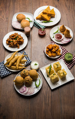Indian Tea time snacks  in group includes Veg Samosa, Kachori/kachaudi, aloo bonda, khaman dhokla, bread, onion,chilli and moong pakora/pakoda/bhaji/bhajji/Bhajiya/bajji with sauces, selective focus