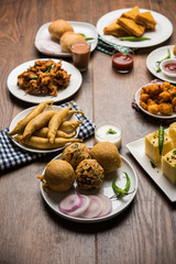 Indian Tea time snacks  in group includes Veg Samosa, Kachori/kachaudi, aloo bonda, khaman dhokla, bread, onion,chilli and moong pakora/pakoda/bhaji/bhajji/Bhajiya/bajji with sauces, selective focus