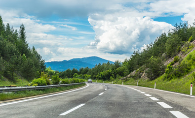 Autobahn or highway in the mountains with clear marking surrounded by vibrant green trees under...