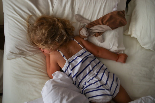 overhead view of toddler sleeping with lovey in bed wearing striped pj