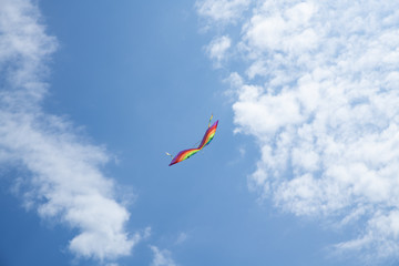 Multicolored kite on the background of the blue sky with clouds