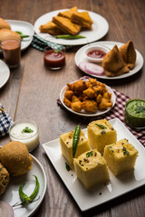 Indian Tea time snacks  in group includes Veg Samosa, Kachori/kachaudi, aloo bonda, khaman dhokla, bread, onion,chilli and moong pakora/pakoda/bhaji/bhajji/Bhajiya/bajji with sauces, selective focus