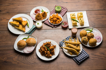 Indian Tea time snacks  in group includes Veg Samosa, Kachori/kachaudi, aloo bonda, khaman dhokla, bread, onion,chilli and moong pakora/pakoda/bhaji/bhajji/Bhajiya/bajji with sauces, selective focus