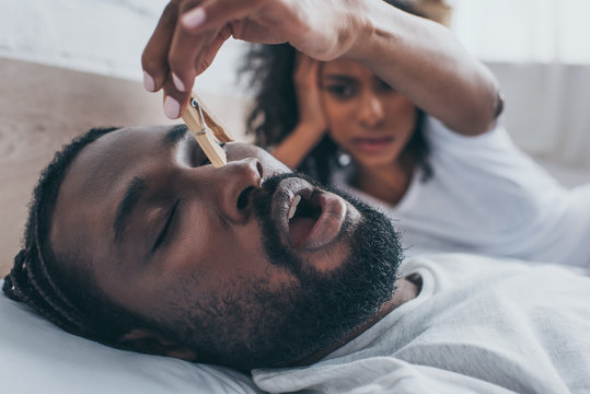 selective focus of snoring african american man near wife holding wooden pin