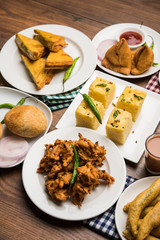 Indian Tea time snacks  in group includes Veg Samosa, Kachori/kachaudi, aloo bonda, khaman dhokla, bread, onion,chilli and moong pakora/pakoda/bhaji/bhajji/Bhajiya/bajji with sauces, selective focus