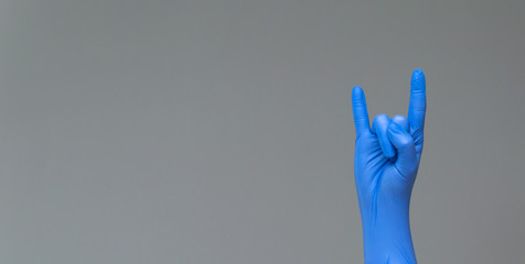 Hand in latex surgical glove, showing the gesture of fans of heavy metal on grey background