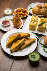 Indian Tea time snacks  in group includes Veg Samosa, Kachori/kachaudi, aloo bonda, khaman dhokla, bread, onion,chilli and moong pakora/pakoda/bhaji/bhajji/Bhajiya/bajji with sauces, selective focus