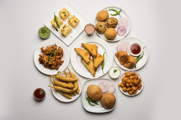 Indian Tea time snacks  in group includes Veg Samosa, Kachori/kachaudi, aloo bonda, khaman dhokla, bread, onion,chilli and moong pakora/pakoda/bhaji/bhajji/Bhajiya/bajji with sauces, selective focus