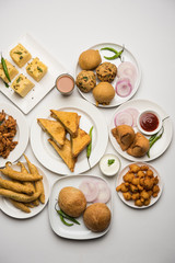 Indian Tea time snacks  in group includes Veg Samosa, Kachori/kachaudi, aloo bonda, khaman dhokla, bread, onion,chilli and moong pakora/pakoda/bhaji/bhajji/Bhajiya/bajji with sauces, selective focus
