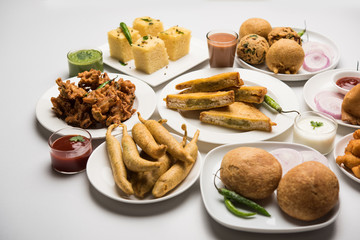 Indian Tea time snacks  in group includes Veg Samosa, Kachori/kachaudi, aloo bonda, khaman dhokla, bread, onion,chilli and moong pakora/pakoda/bhaji/bhajji/Bhajiya/bajji with sauces, selective focus