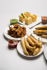Indian Tea time snacks  in group includes Veg Samosa, Kachori/kachaudi, aloo bonda, khaman dhokla, bread, onion,chilli and moong pakora/pakoda/bhaji/bhajji/Bhajiya/bajji with sauces, selective focus