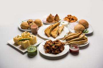 Indian Tea time snacks  in group includes Veg Samosa, Kachori/kachaudi, aloo bonda, khaman dhokla, bread, onion,chilli and moong pakora/pakoda/bhaji/bhajji/Bhajiya/bajji with sauces, selective focus