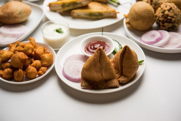 Indian Tea time snacks  in group includes Veg Samosa, Kachori/kachaudi, aloo bonda, khaman dhokla, bread, onion,chilli and moong pakora/pakoda/bhaji/bhajji/Bhajiya/bajji with sauces, selective focus