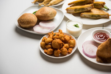Indian Tea time snacks  in group includes Veg Samosa, Kachori/kachaudi, aloo bonda, khaman dhokla, bread, onion,chilli and moong pakora/pakoda/bhaji/bhajji/Bhajiya/bajji with sauces, selective focus