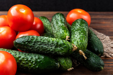 Fresh cucumbers and tomatoes on dark wooden background.