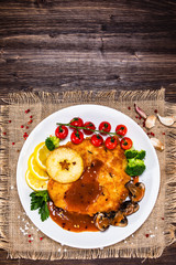 Fried pork chop with vegetables and mushrooms on wooden background