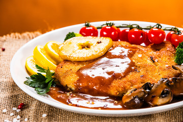 Fried pork chop with vegetables and mushrooms on wooden background