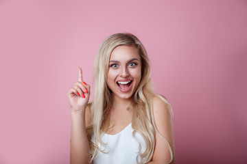 Beautiful girl with blond hair pointing to looking up on pink background. Presenting your product