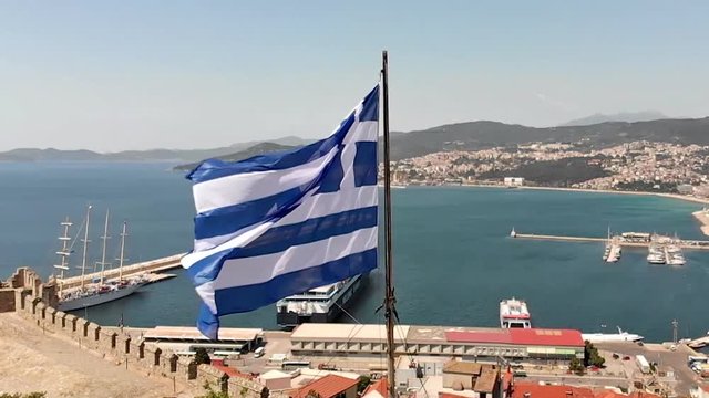 Greek flag waving in slow motion, orbit shot. Kavala city port