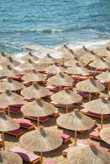 Many reed straw umbrellas with sun loungers on a beautiful sandy beach on the Adriatic coast, an aerial top view 