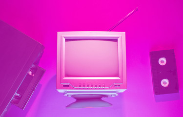 Retro wave, 80s concept. Video player with vhs cassette, old tv, neon pink light. Top view, flat lay