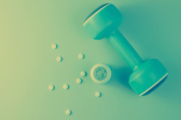 Minimalism sports pharmacology concept. Blue plastic dumbbell and bottle with white vitamin pills,...