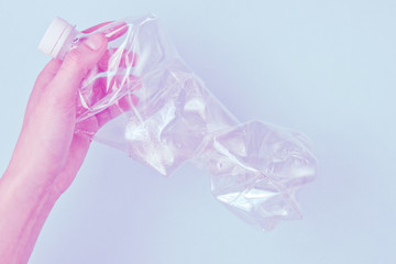 Minimalistic pollution ecology concept. Female hands twists rumpled plastic bottle. Tonned photo....