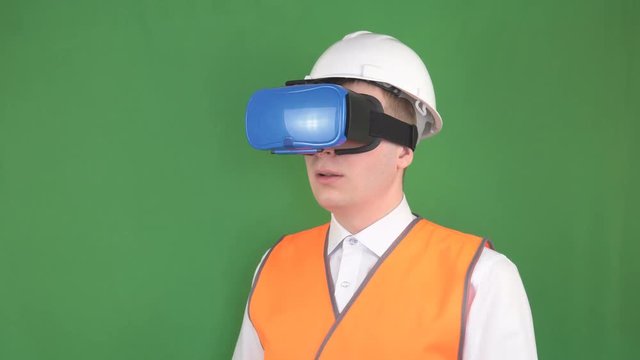 A male caucasian engineer wearing virtual reality glasses at a construction site, new modern technologies, green background, chromakey