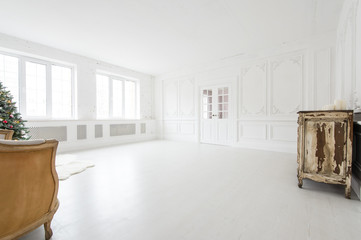 Luxurious bright interior with stucco walls, christmas tree, vintage chest of drawers and sofa.