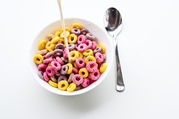 Milk is poured into a bowl with multi-colored round-shaped flakes.