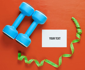 Sport weight loss concept. Dumbbells, ruler, pills on orange background. Minimalism. White sheet of paper for copy space. Top view