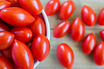 small bowl overflowing with bright red grape tomatoes on a wood background viewed from above