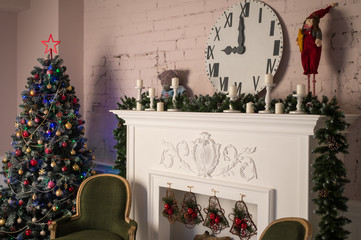 White fireplace with stucco patterns, candles, wach face, fir branches. Christmas decor. Close up. Selective focus.