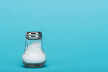 glass salt shaker full of salt on blue background with copy space