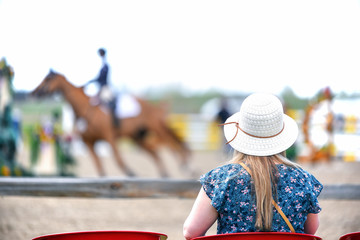 Female wearing hat watching horse jumping competition