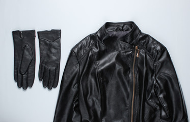 Fashionable women's clothing and accessories. Leather jacket, gloves on gray background. Top view