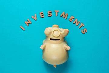 Piggy bank on blue background with text investments with letters. Top view. Minimalistic business concept