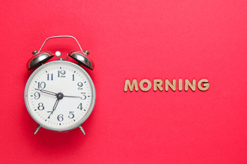 Retro alarm clock on red background with text morning with letters.