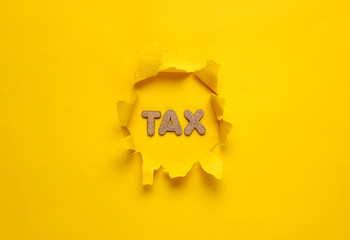 The word tax in a torn hole of yellow background. Top view