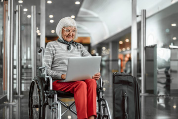 Joyful mature lady on disabled carriage with luggage at airport