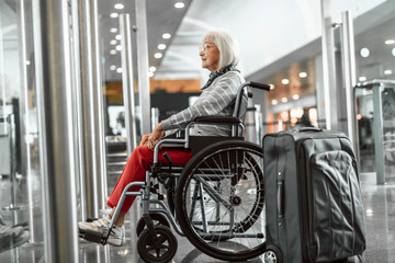Fototapeta na wymiar Smiling mature lady on disabled carriage looking forward at airport