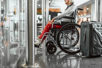 Obraz premium Smiling mature lady on disabled carriage waiting for trip at airport