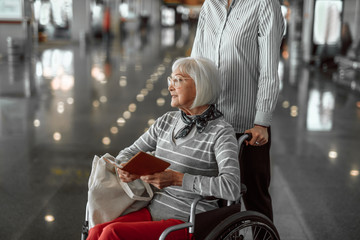 Female worker of airport helping elderly woman in wheelchair at hall