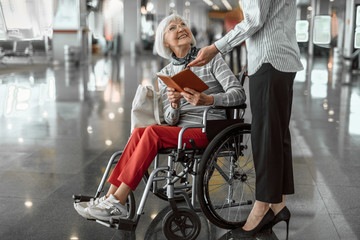 Female worker of airport talking to elderly woman in wheelchair at hall