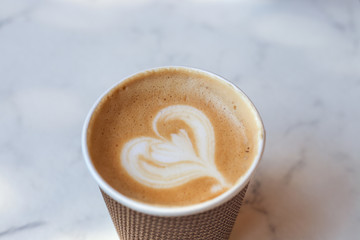 black coffee with cream in the shape of a heart is in a brown paper cup on a table in a cafe