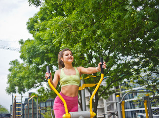 Attractive athletic woman doing exercises on exercise machines on the sports ground outdoors